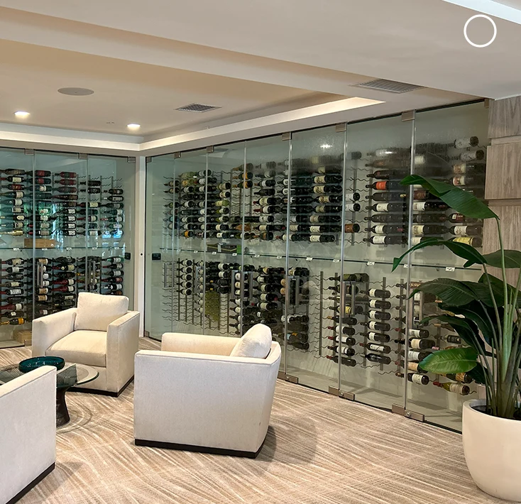 Glass wine storage wall, modern interior design with comfy chairs, perfect for luxury homes or restaurants.