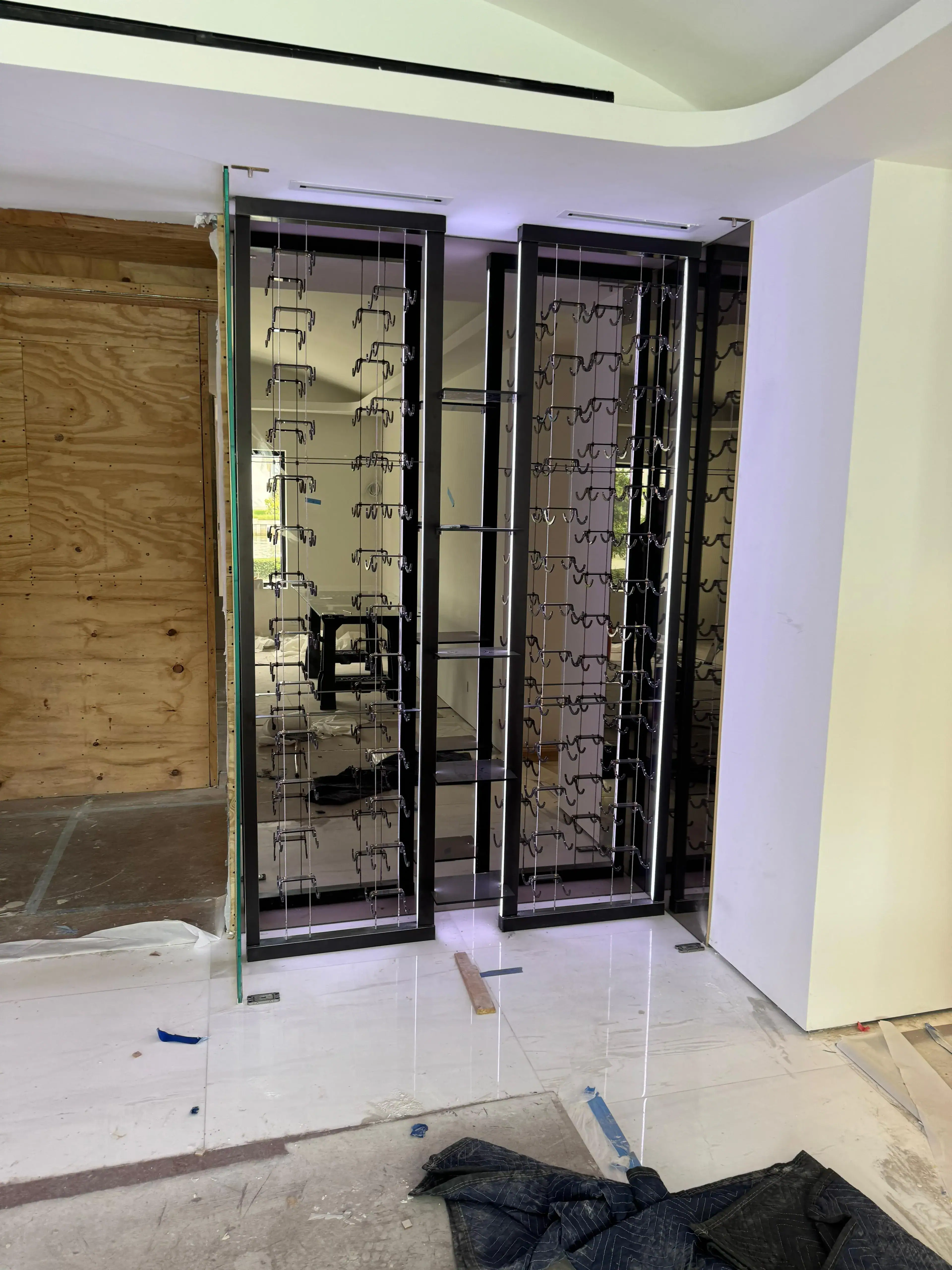 ALT: Modern black-framed glass wine rack with metal hooks for bottles and cocktails.