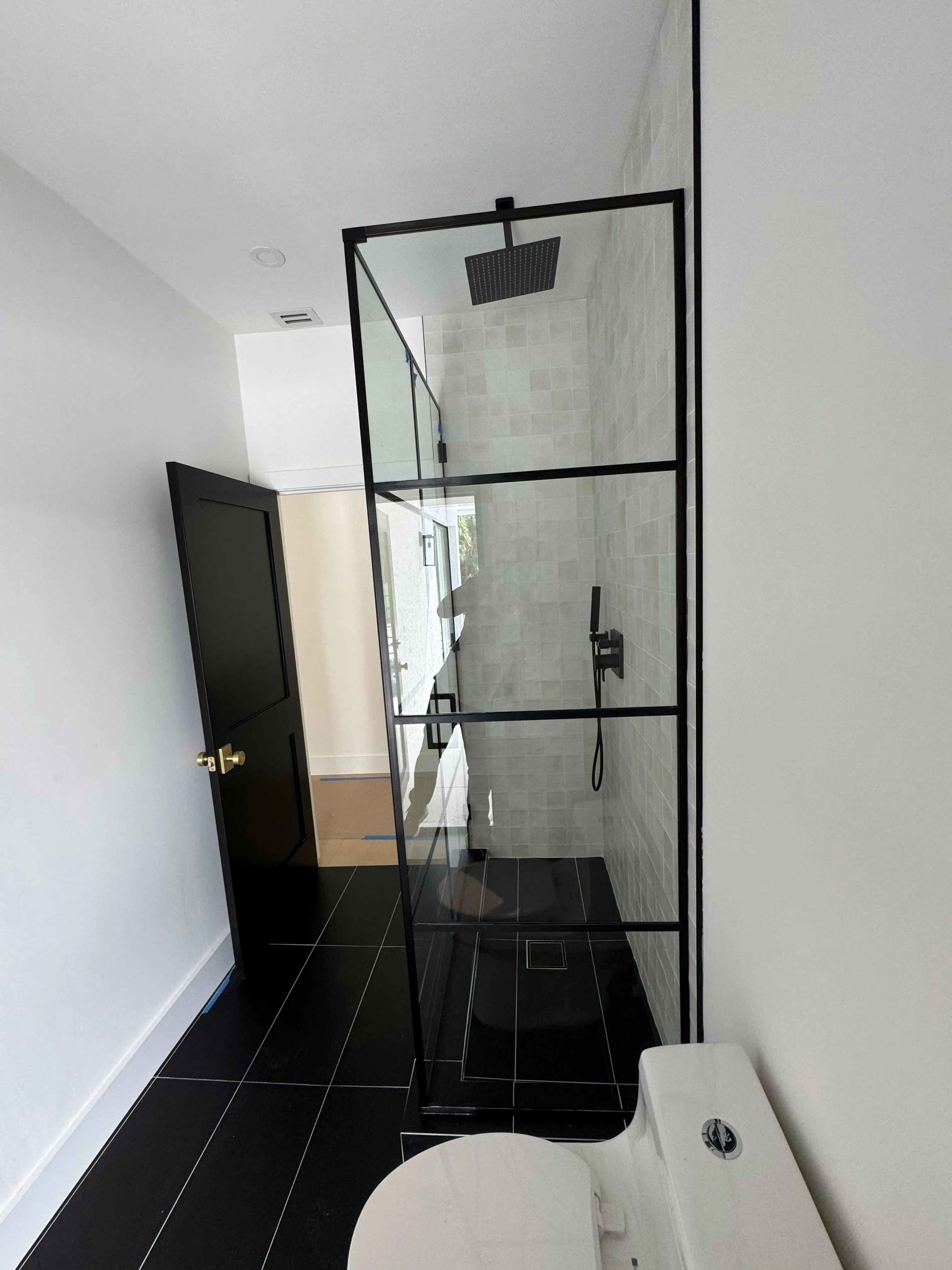 Elegant glass shower door with black metal frame, tiled shower interior, rainfall showerhead for luxury bathroom upgrade.