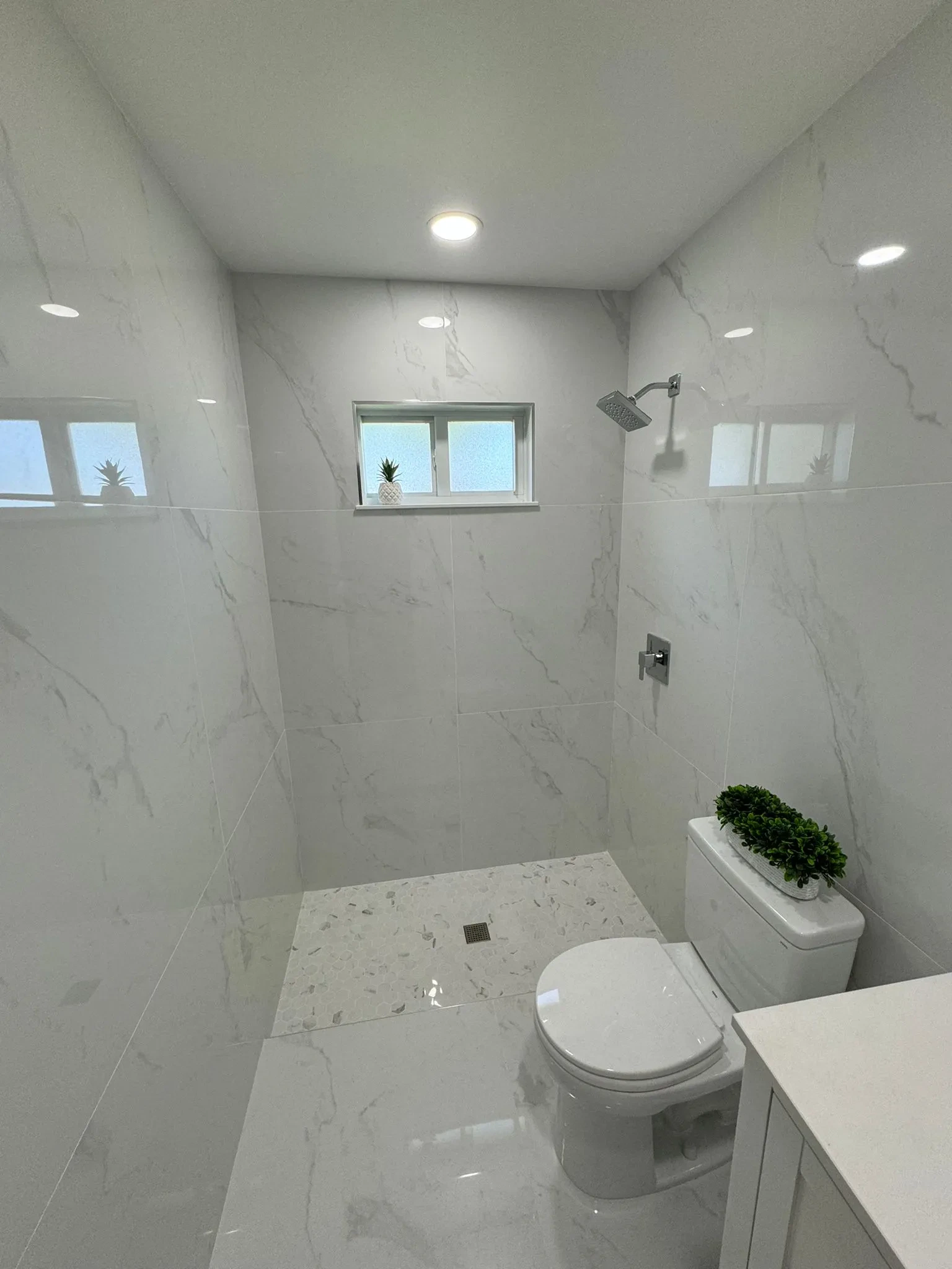 Modern marble-tiled bathroom featuring a mirror, glass shower, and minimal decor for luxury styling.