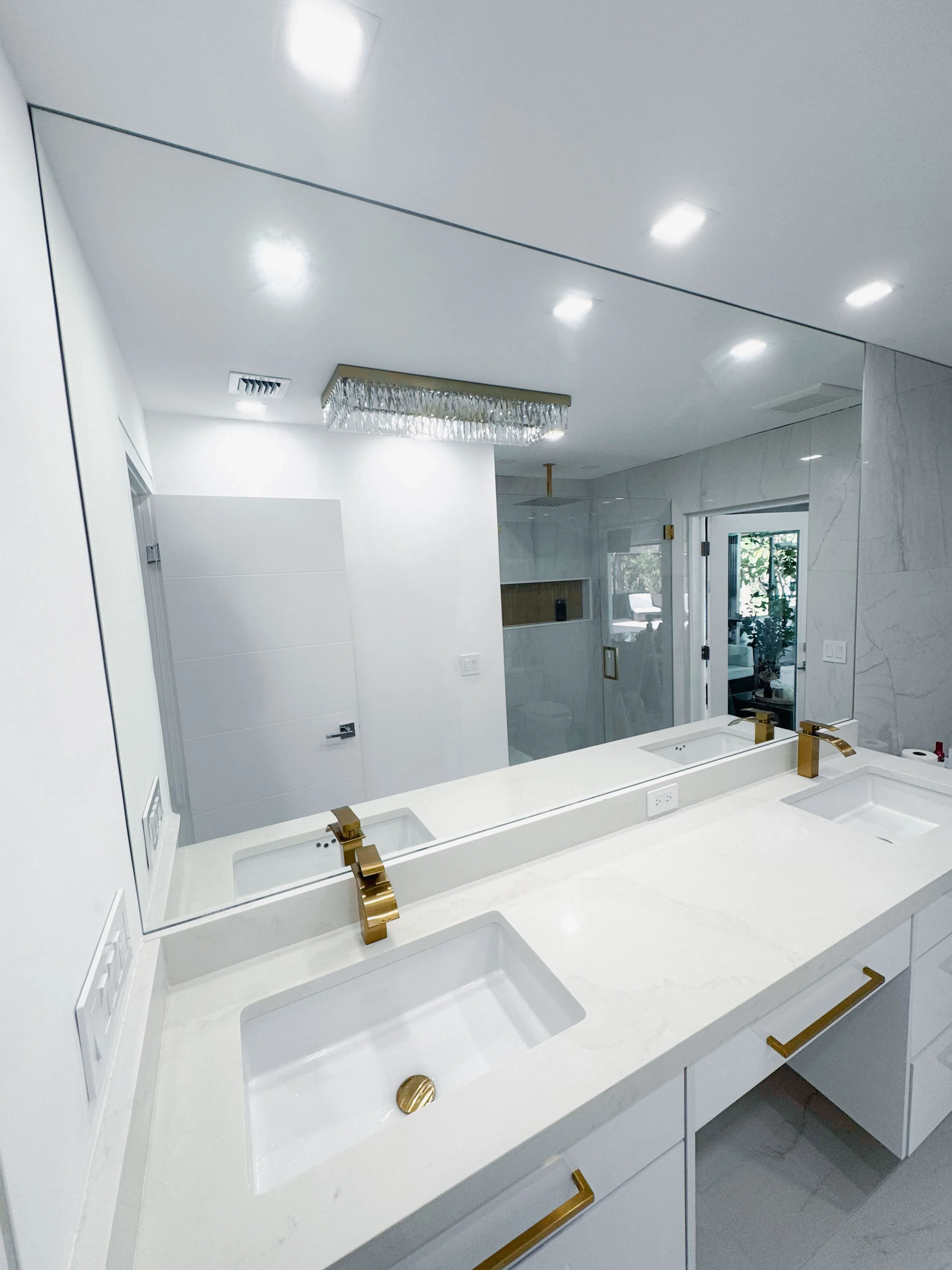 Alt text: Modern bathroom mirror with double sinks and gold fixtures in a bright, white space.