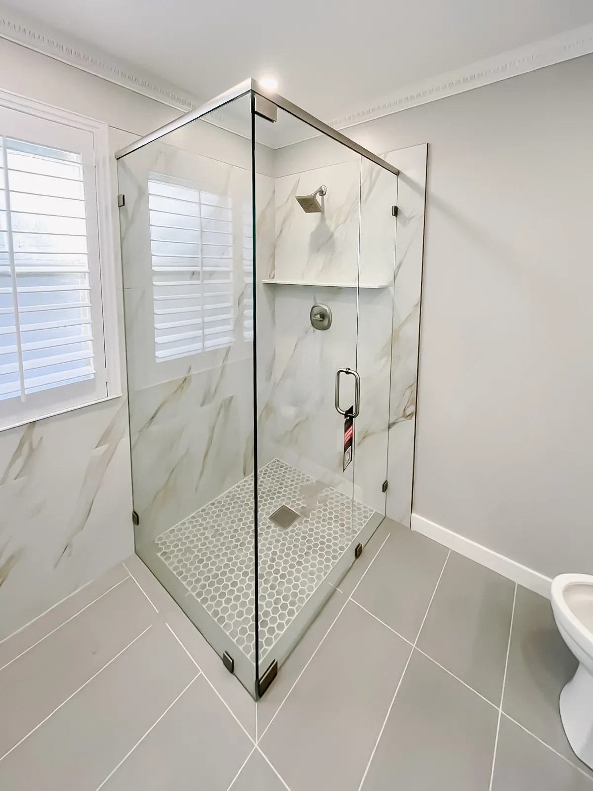 High-quality glass shower door with sleek steel hardware and marble wall accents for luxurious bathroom design.