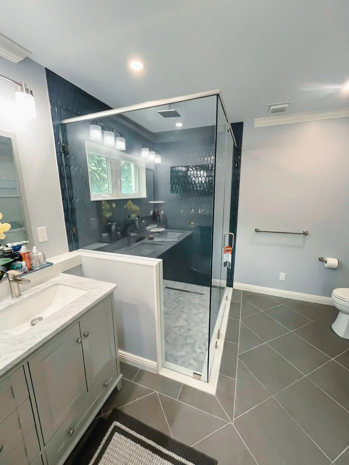 Highly reflective glass shower with sleek black tiles, contemporary bathroom decor, and multiple light fixtures.