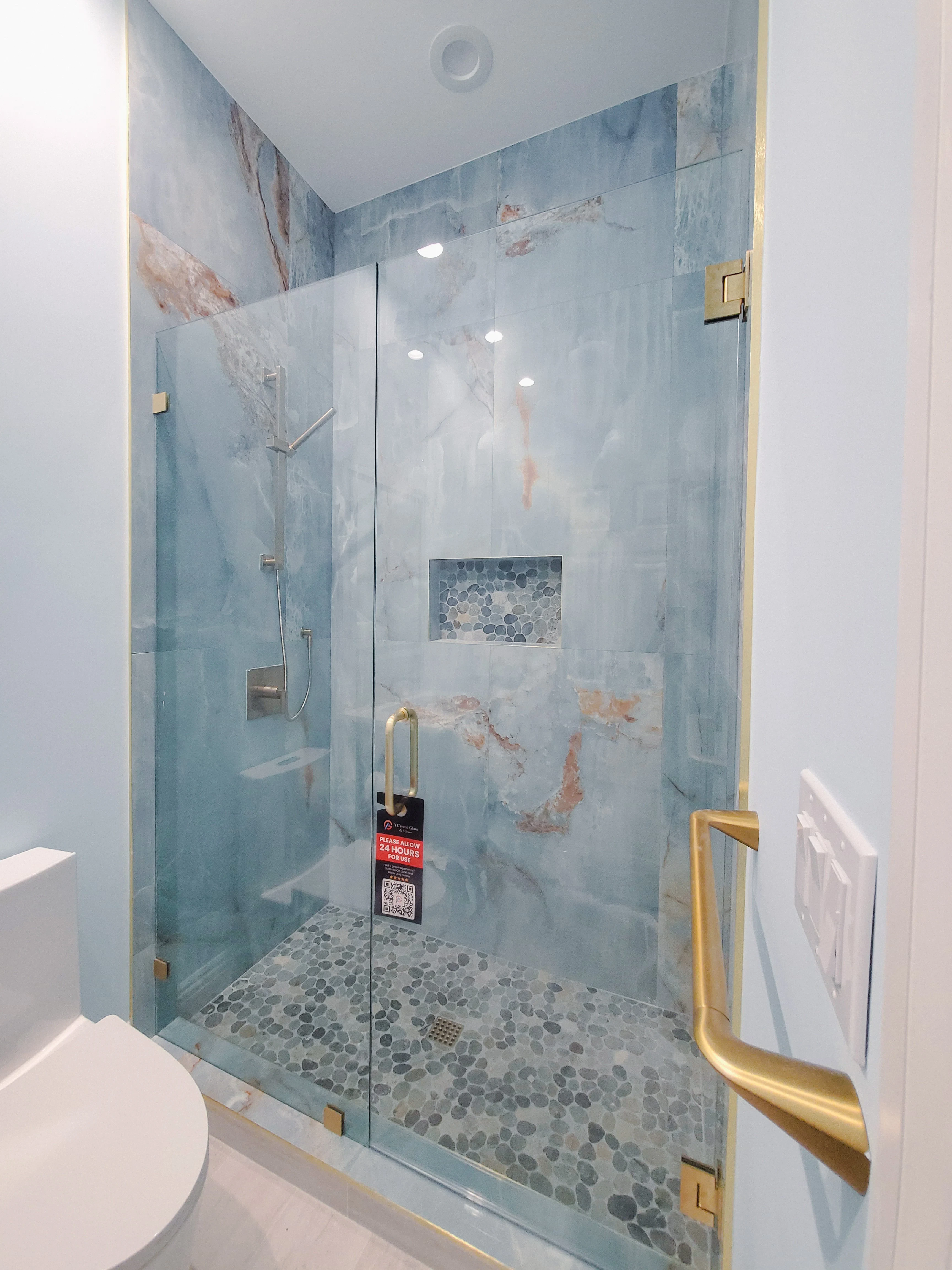 High-quality glass shower with marble tiles and brushed gold fixtures for luxury bathroom design.