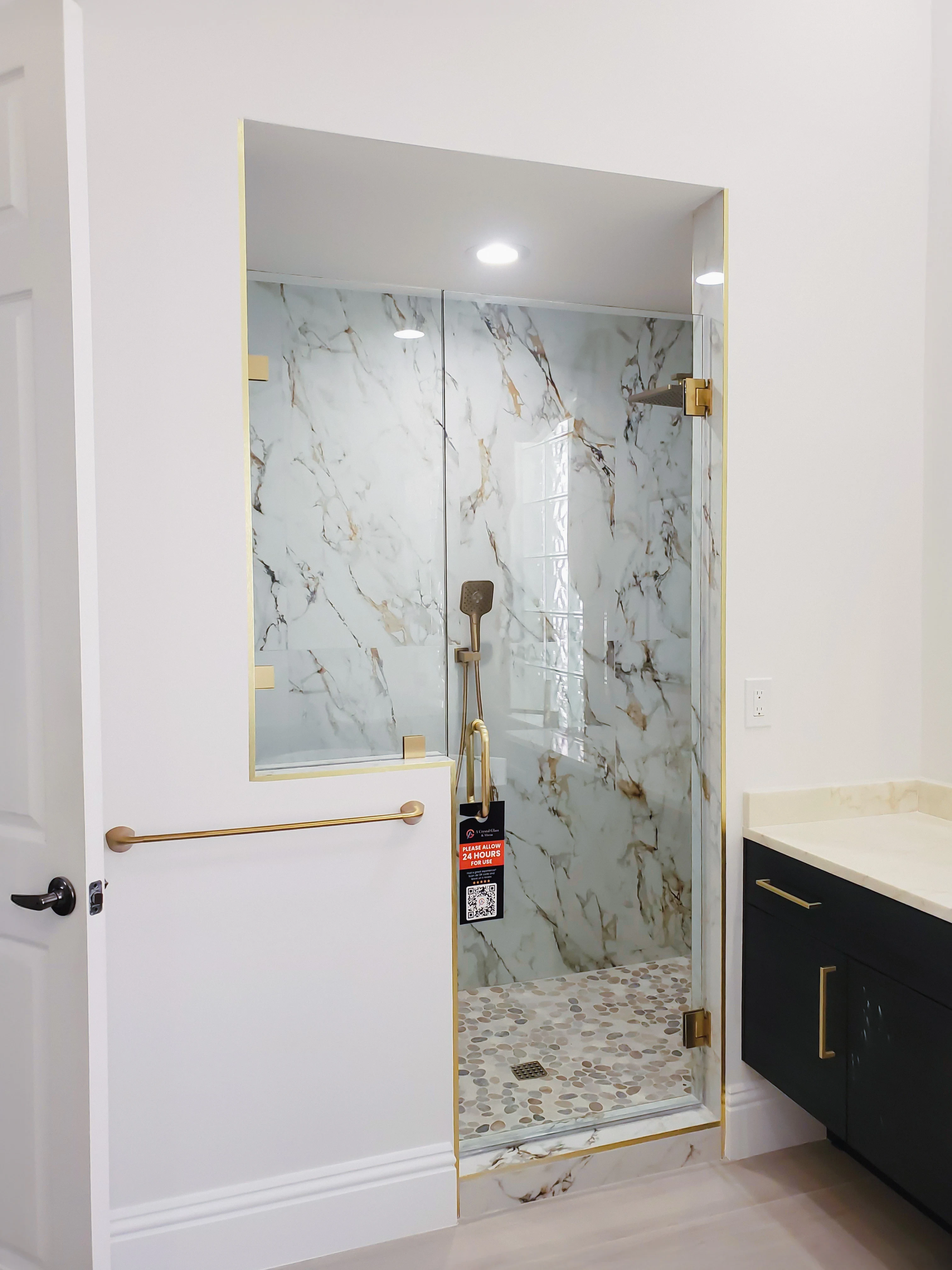 High-quality glass shower enclosure with marble walls and pebble floor, stylish gold accents, and modern design.