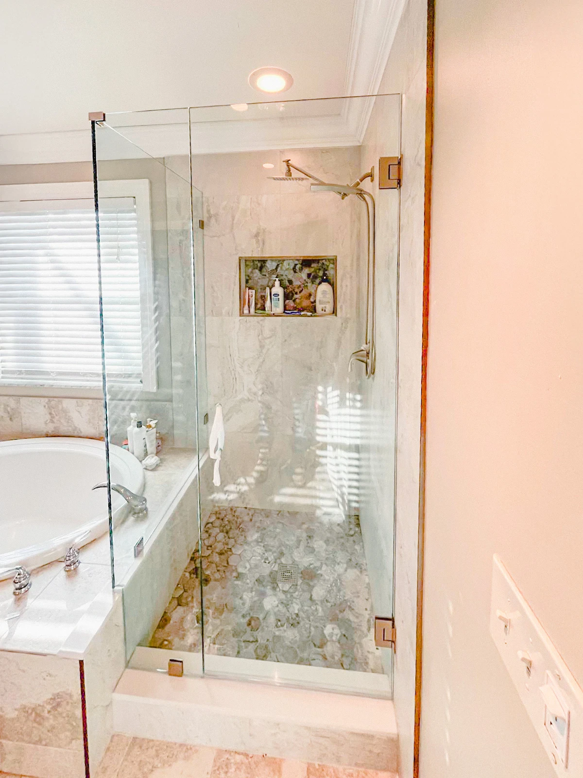 Clear glass shower door with brass hardware, showcasing a sleek design in a luxurious bathroom setting.