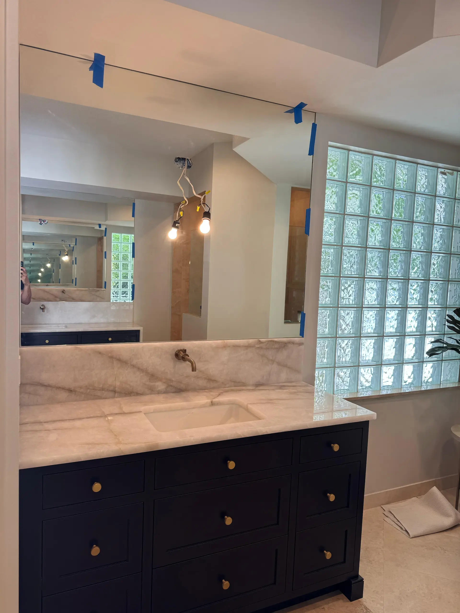 Bright bathroom with custom mirror, marble vanity, glass block window, and modern lighting, showcasing high-quality glass and mirror craftsmanship.