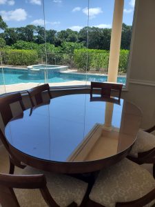 Elegant glass table with wooden chairs overlooking pool and lush greenery.