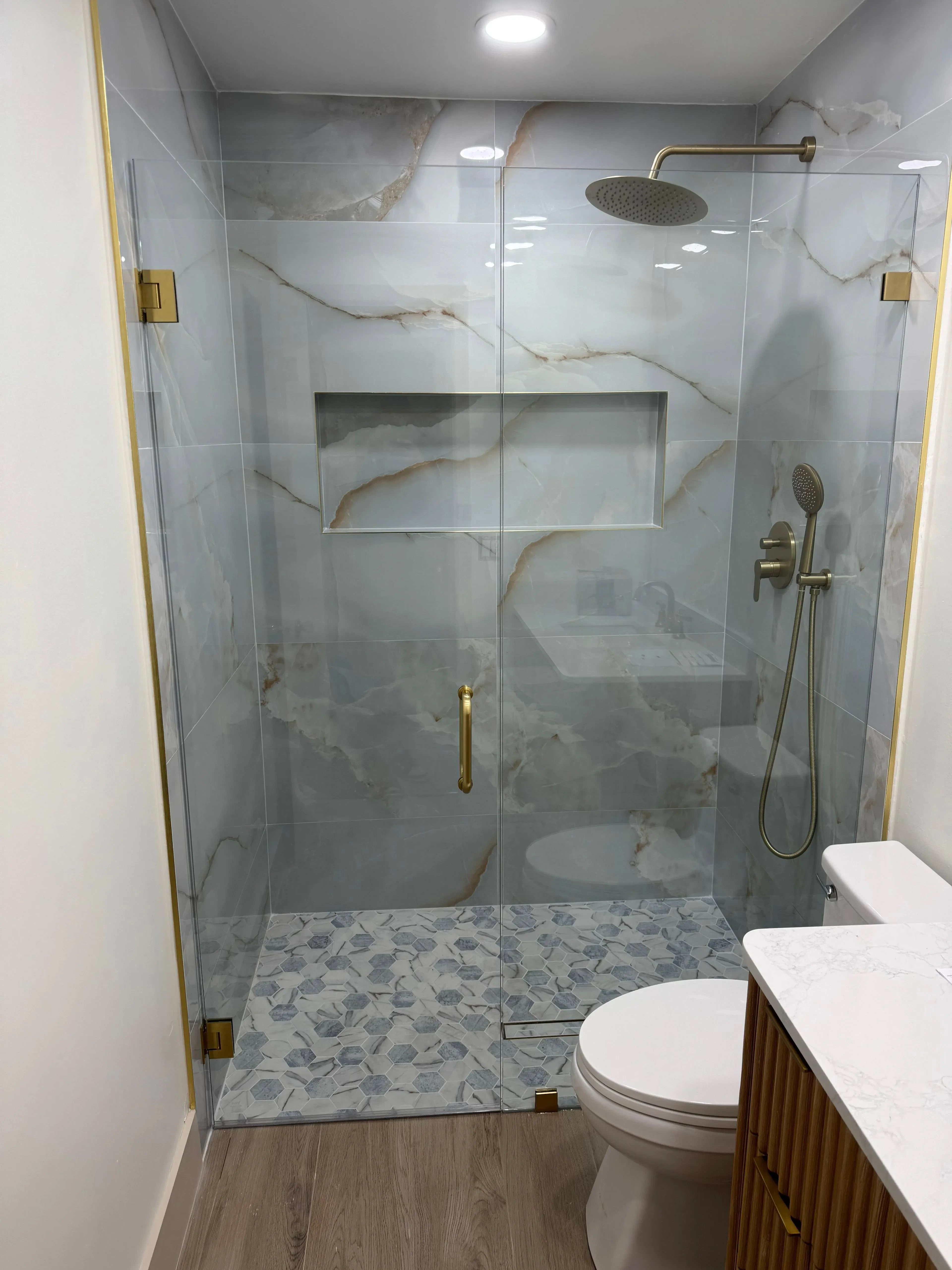 High-quality glass shower door with gold hardware, marble tile walls, and stylish pebble stone floor.