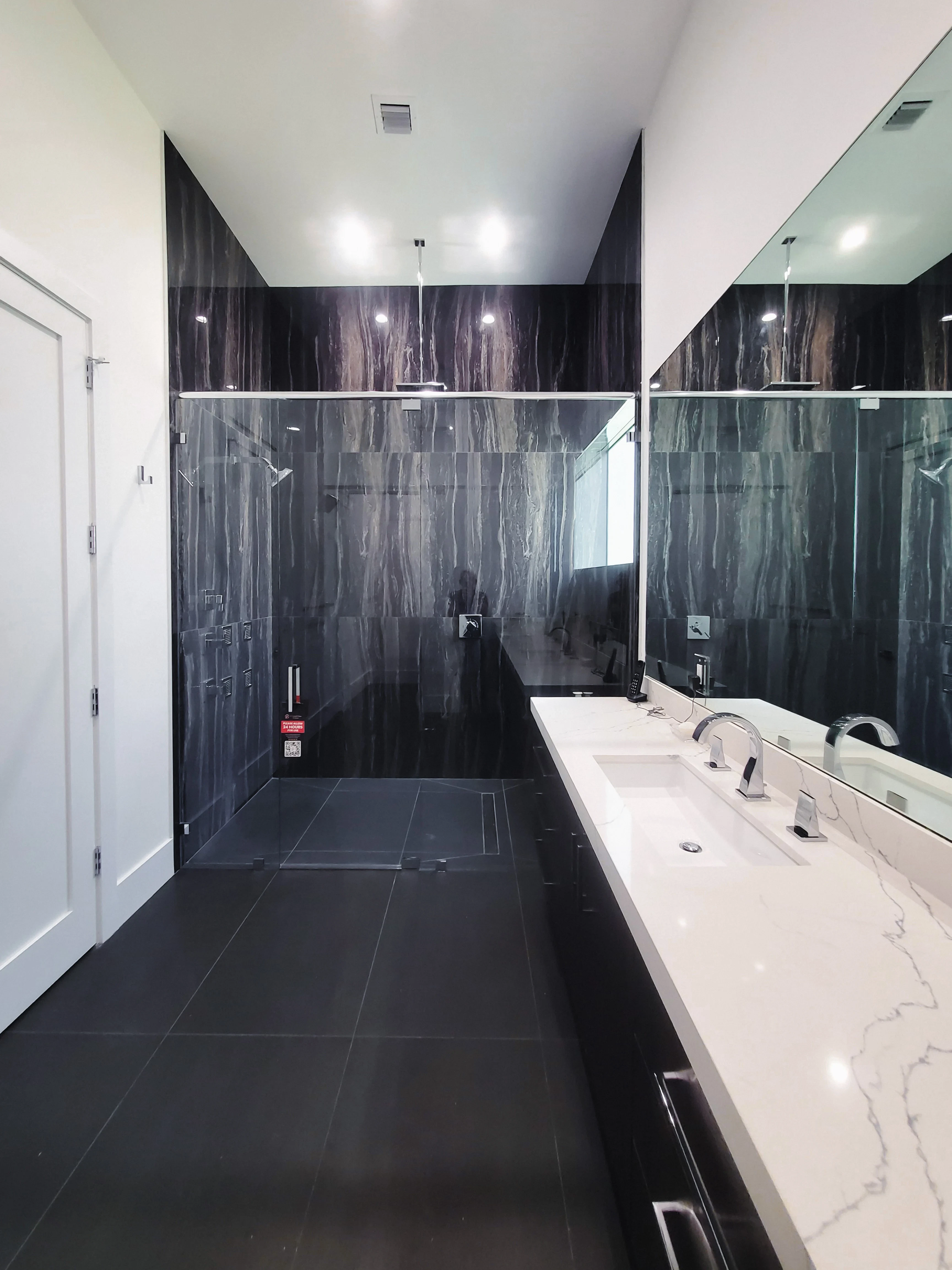 Mirror image of modern hotel bathroom with black marble walls and white vanity.