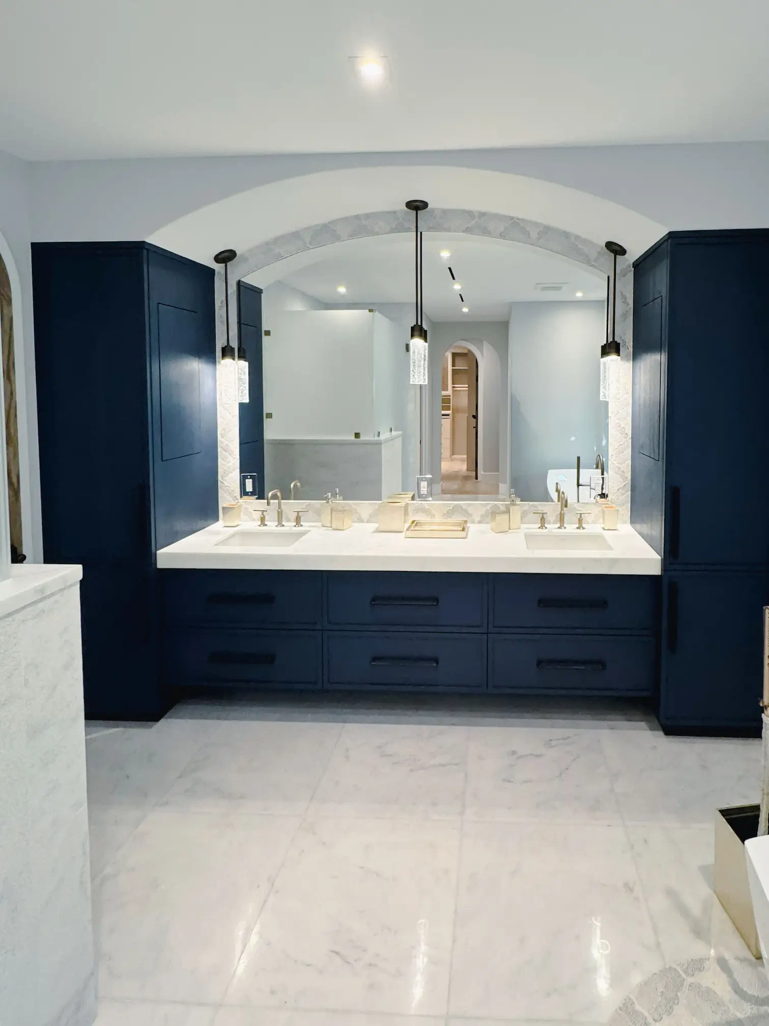 Luxurious glass mirror and marble bathroom vanity with navy cabinetry and chic lighting fixtures.