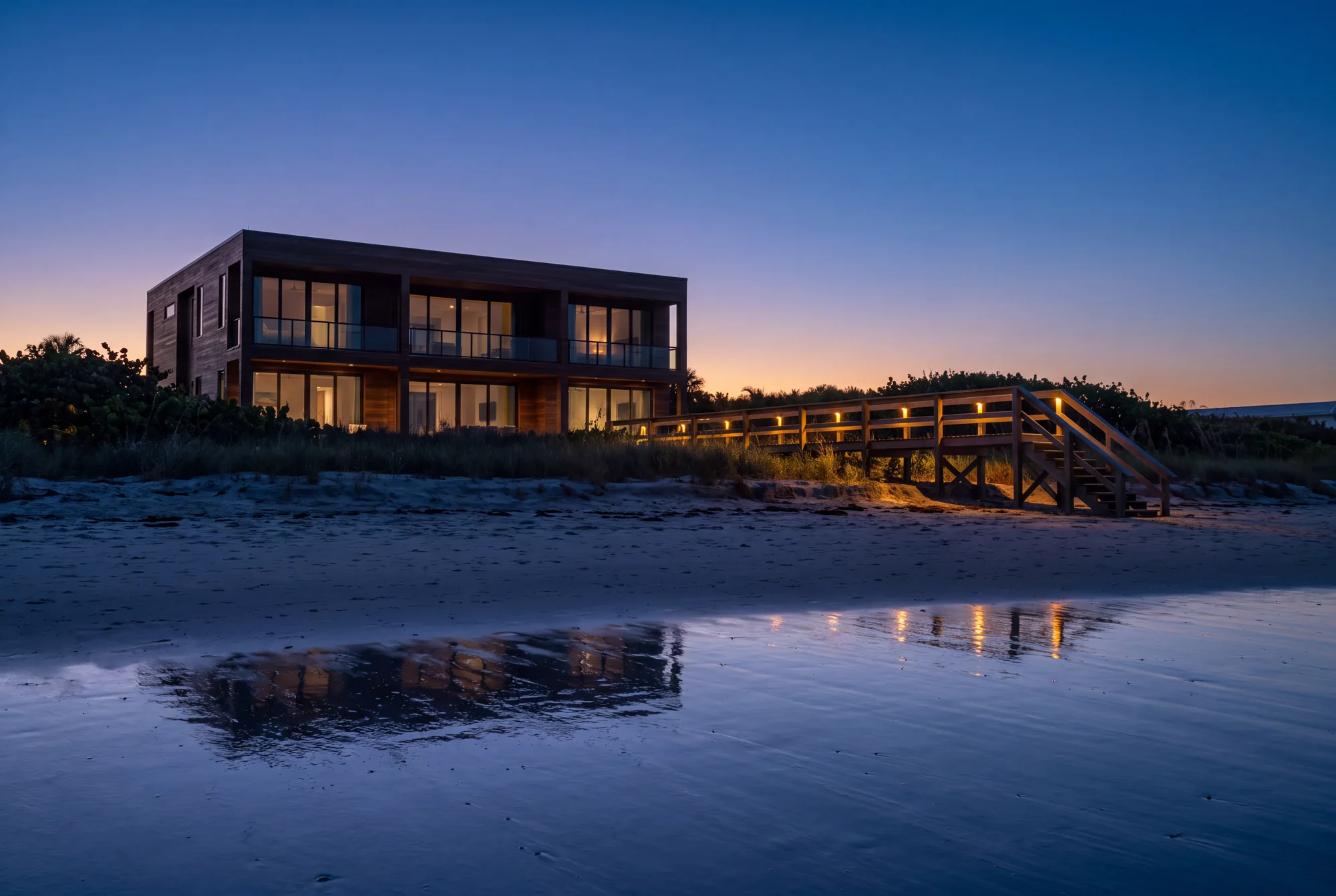 Oceanfront South Florida home at dusk seen from the beach, warm interior light contained behind tinted impact glass