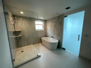 High-quality glass shower enclosure and modern free-standing tub in a sleek, marble-tiled bathroom.