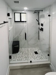 Modern black-framed glass shower with marble walls, pebble floor, and sleek fixtures for luxury bathroom design.