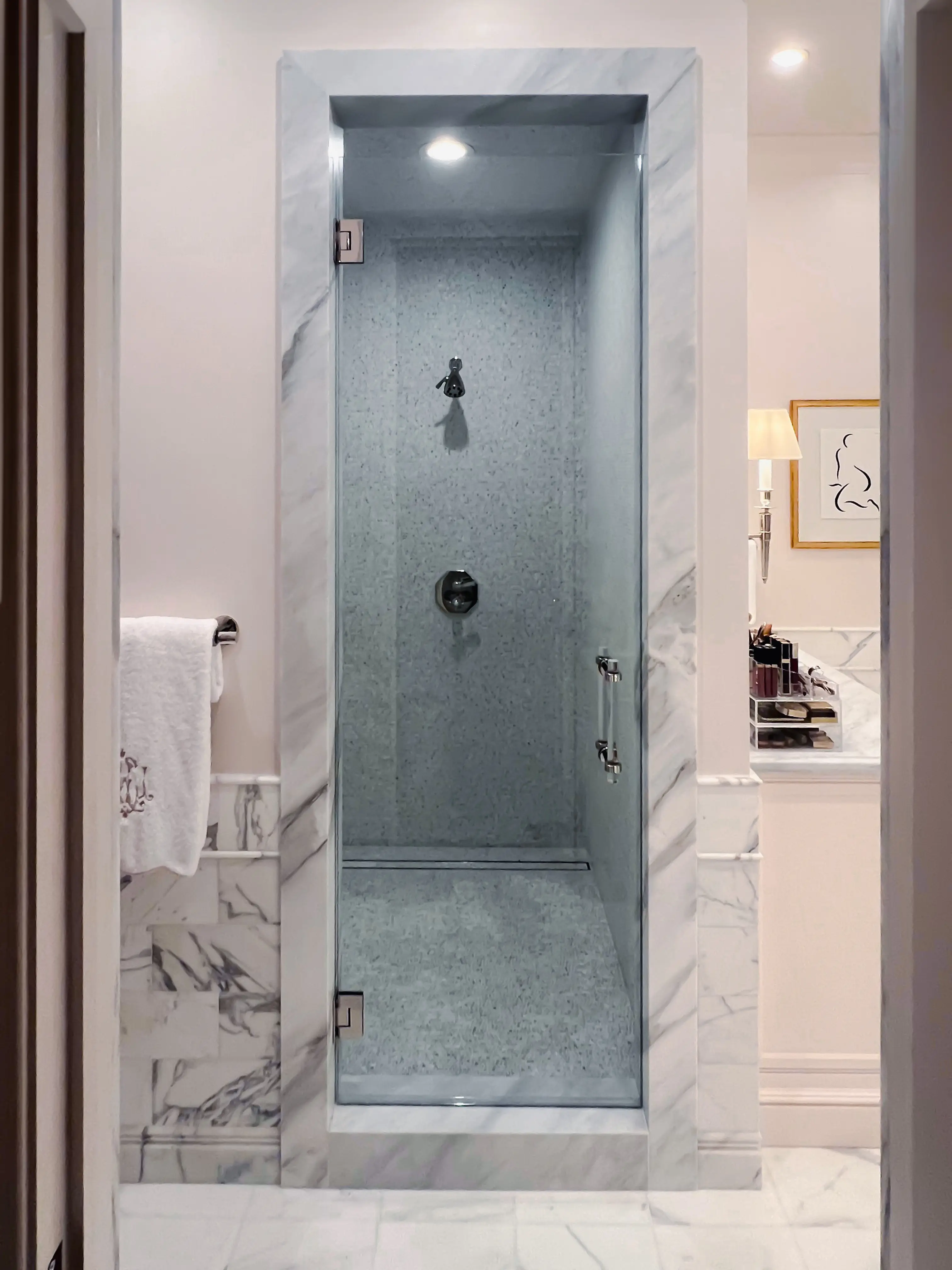 Clear glass shower door with marble frame in luxurious bathroom setting.