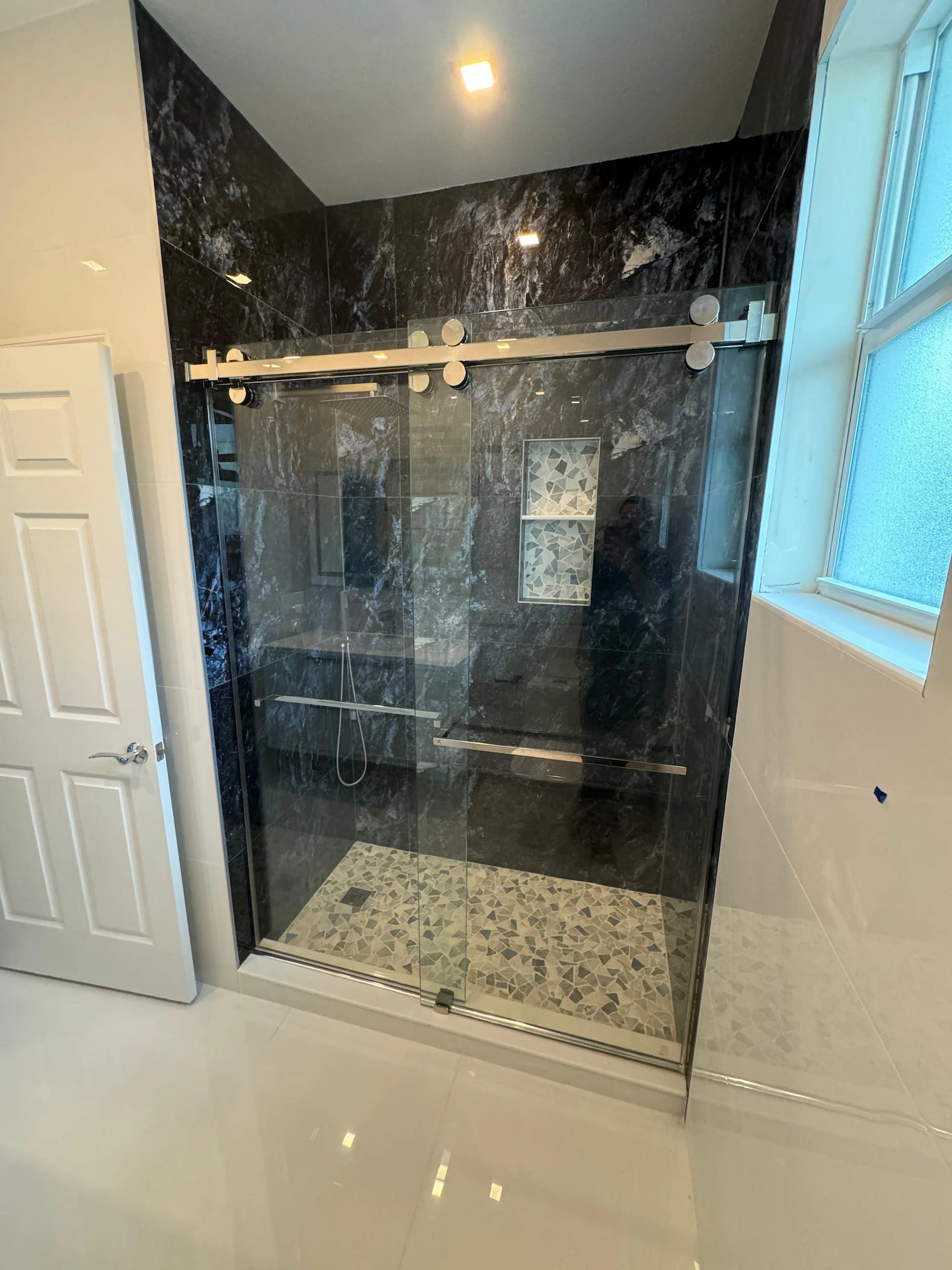 Modern glass shower enclosure with sliding door and black marble walls.