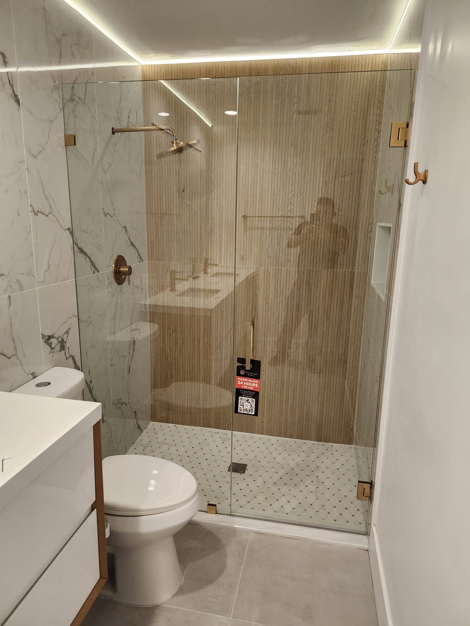 Modern bathroom glass shower with wood paneling, marble walls, and sleek fixtures.