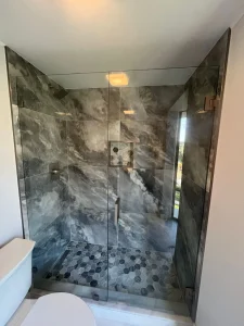 Luxury glass shower with marble walls and hex tile flooring, premium mirror finish.