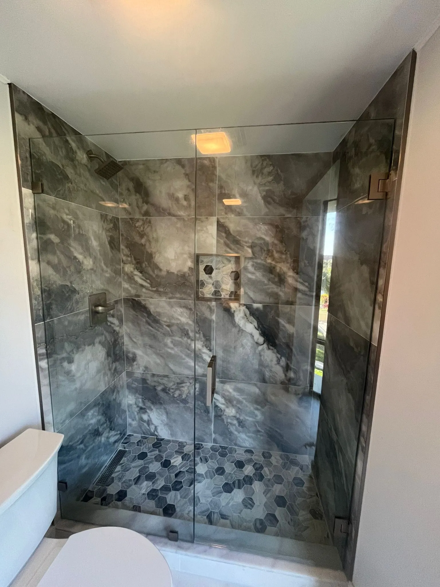 Luxury glass shower with marble walls and hex tile flooring, premium mirror finish.