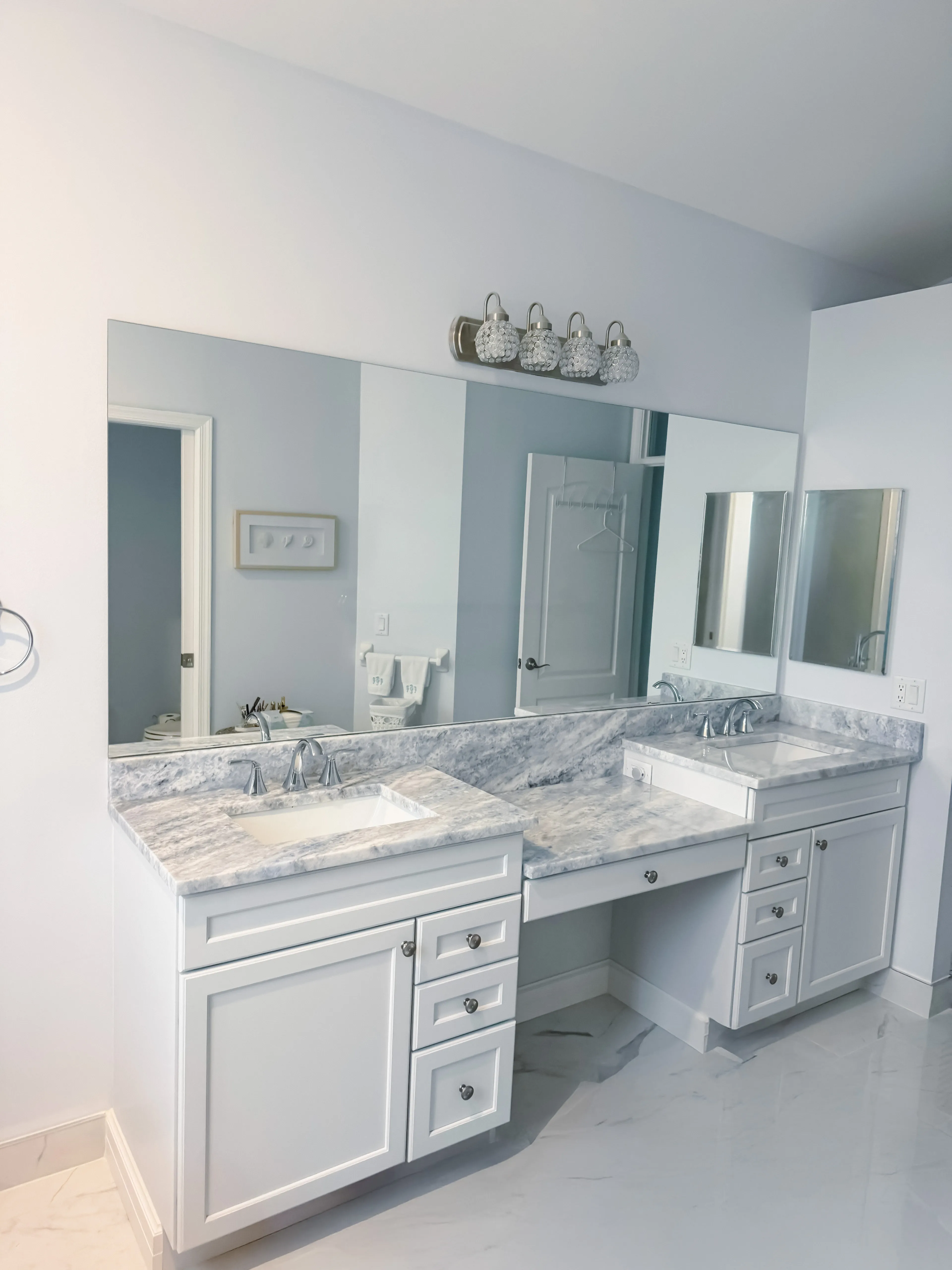 Bright bathroom featuring a white double vanity with marble countertops and mirrored cabinets.