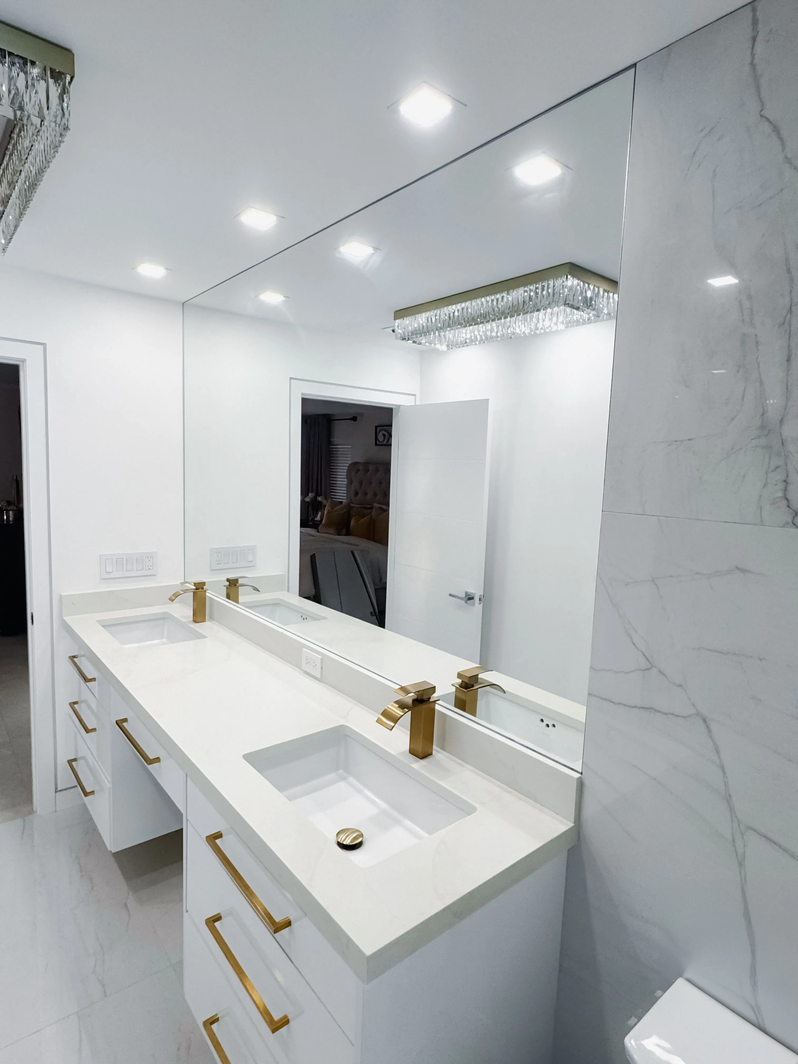Luxury glass and mirror bathroom with sleek white surfaces and gold hardware.