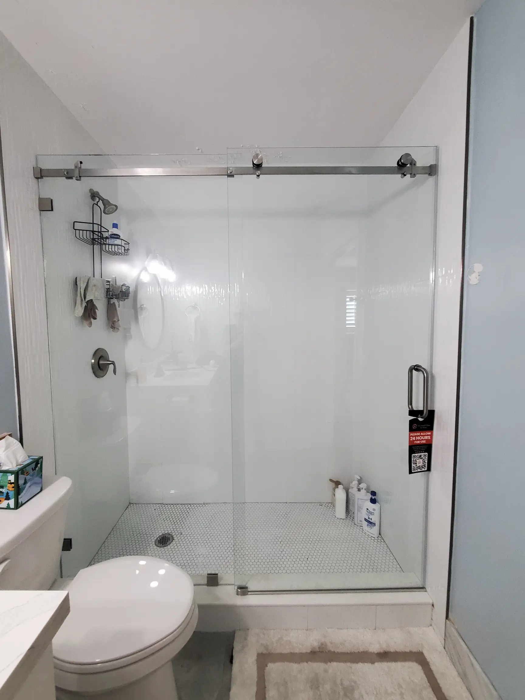 The image showcases a modern glass shower enclosure with a sliding door and brushed nickel hardware. It features built-in shower accessories and a minimalist design.