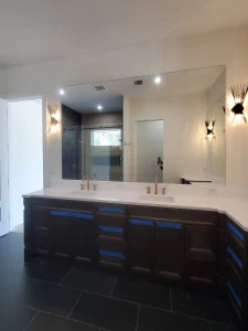 Bright bathroom with large wall mirror, dual sinks, and modern lighting.