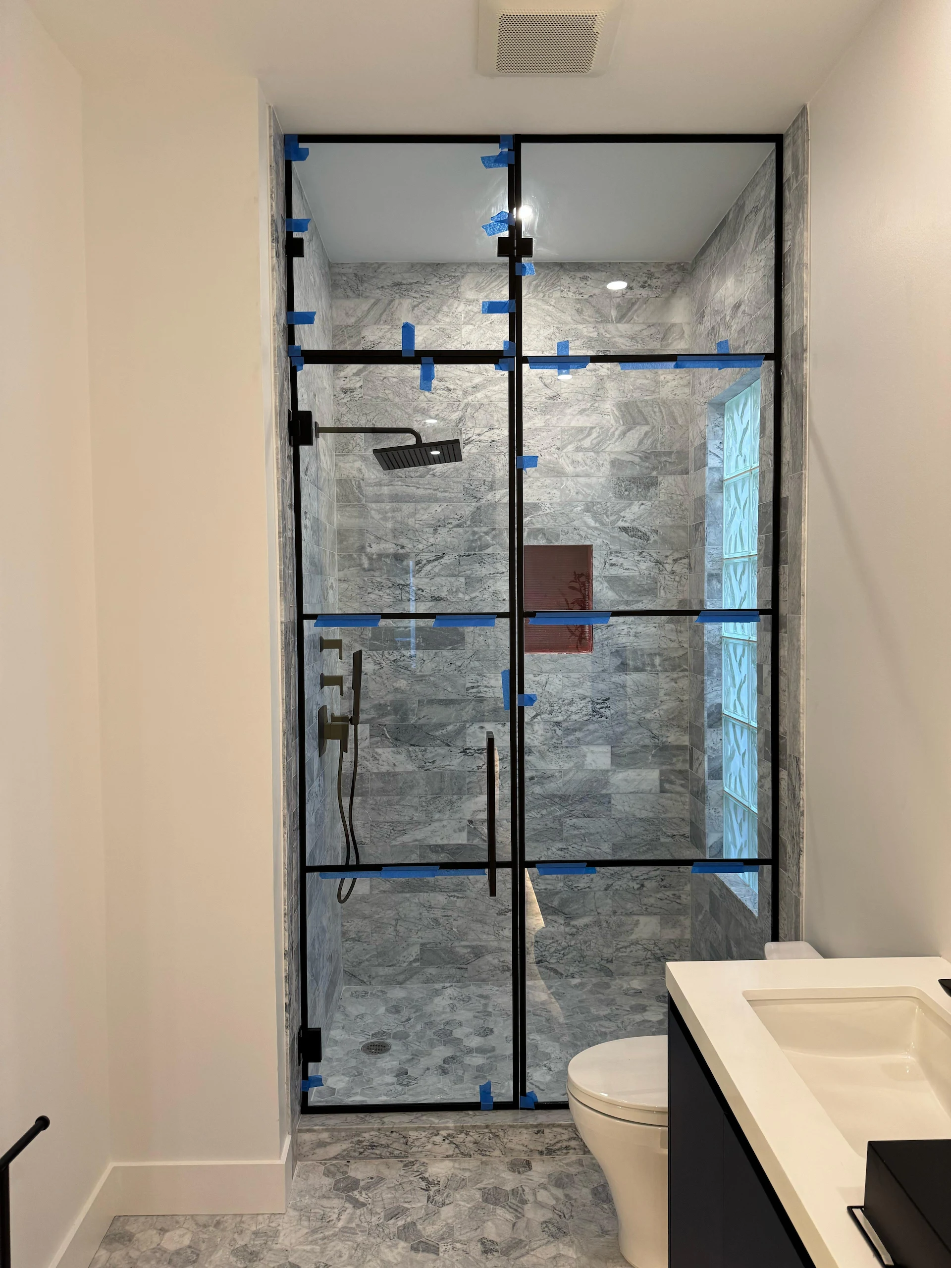 Elegant bathroom with clear glass shower partition, marble tiles, black frame, and contemporary fixtures.