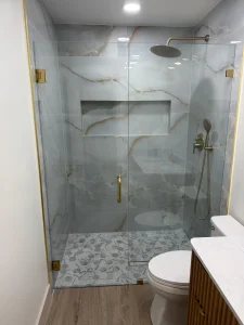 High-quality glass shower door with gold hardware, marble tile walls, and stylish pebble stone floor.