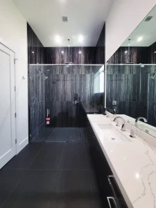 Mirror image of modern hotel bathroom with black marble walls and white vanity.