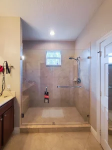 Clear glass shower door with ADA grab bar and tile walls.