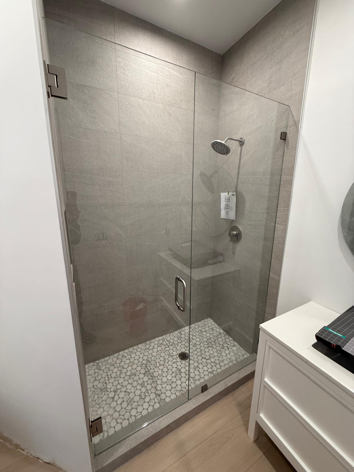 Alt text: Modern glass shower with chrome fixtures and pebble floor in a stylish bathroom.