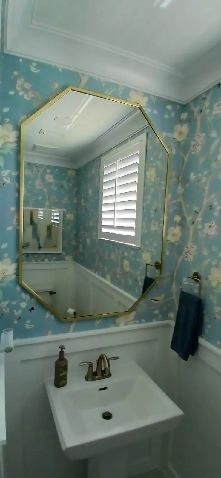 Beautiful octagonal glass mirror with gold frame in a floral-themed bathroom.