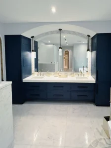 Luxurious glass mirror and marble bathroom vanity with navy cabinetry and chic lighting fixtures.