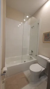 Clear glass bathroom shower partition, modern showerhead, and tub with clean tile design.