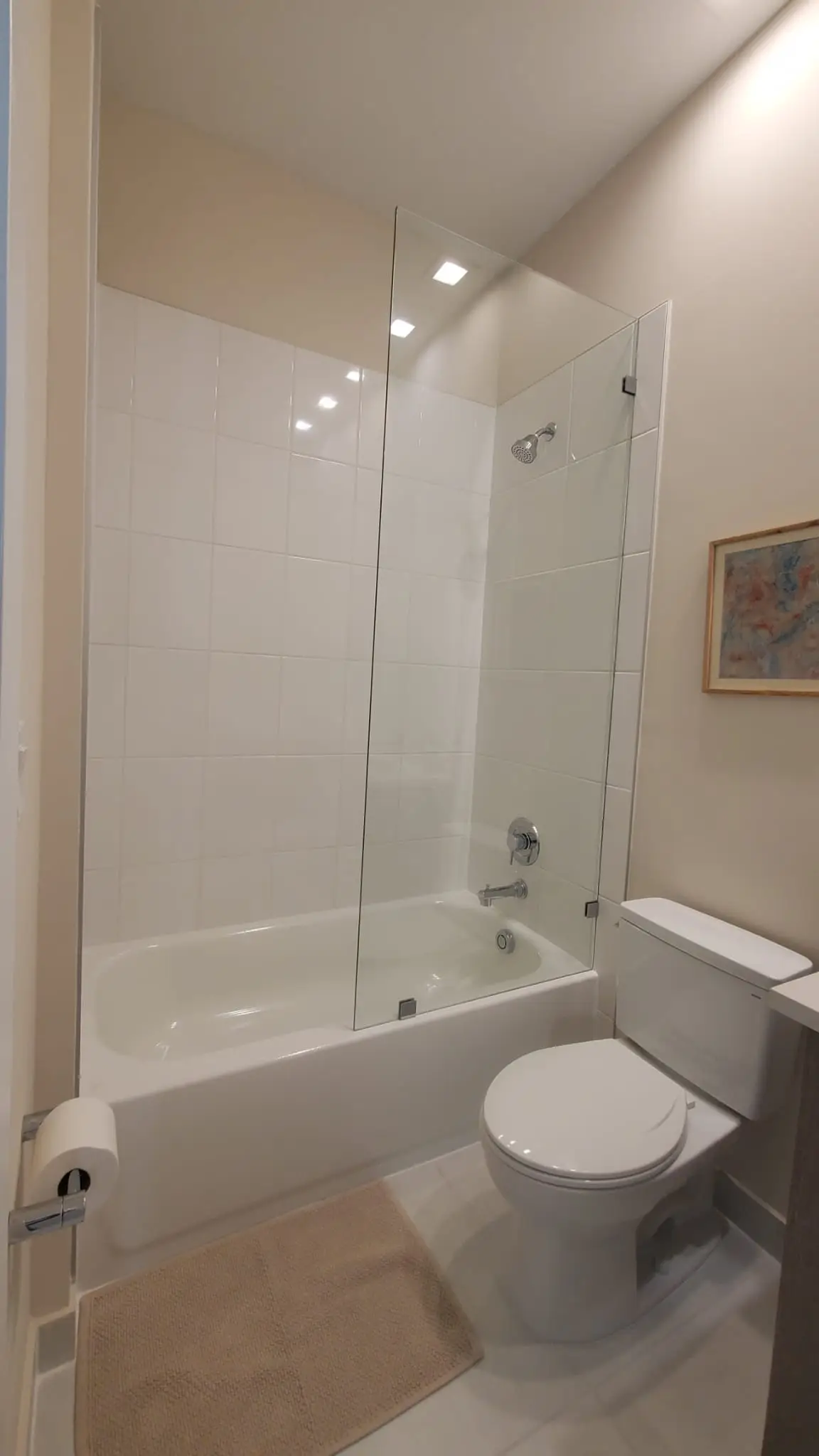 Clear glass bathroom shower partition, modern showerhead, and tub with clean tile design.