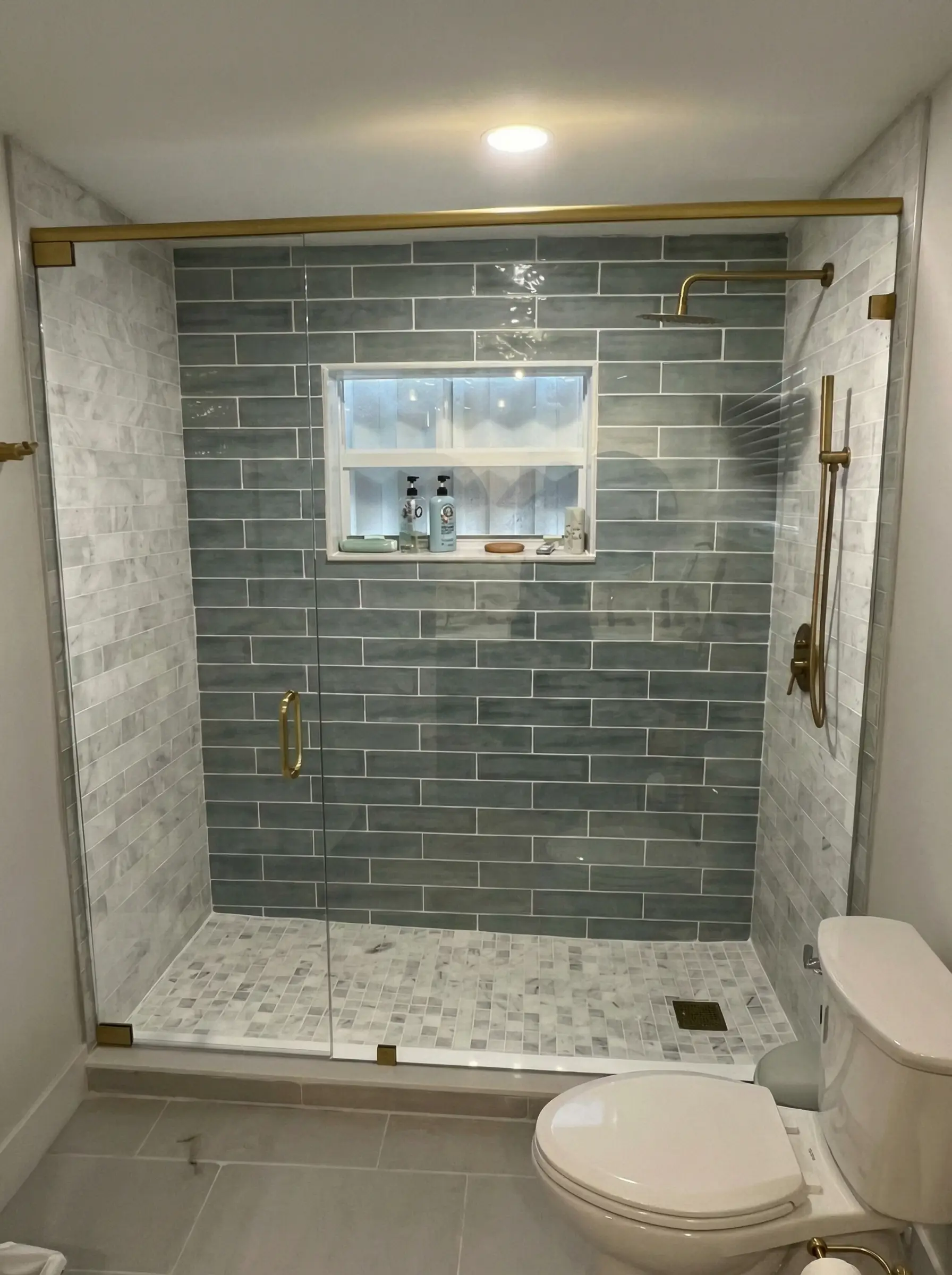 Glass shower enclosure with brass hardware and gray tile walls.