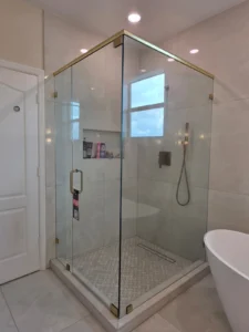 Frameless corner shower enclosure with satin brass header and clamps in a Royal Palm Beach primary bathroom
